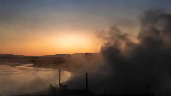 A hot spring is releasing an immense cloud of steam before sunset, right by a lake